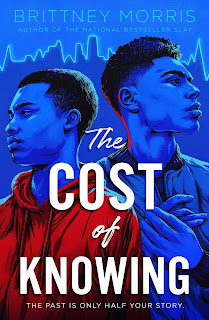 Two black teenagers stand in blue light, one is wearing a bright red hoodie, they face away from each other.