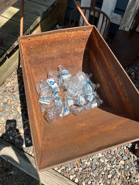Photo of empty plastic water bottles in the bottom of a rusty garden cart.