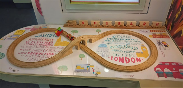 A wooden toy 'Rhubarb Train' set up, on top of artwork designed by Liz Kay about the Rhubarb Train