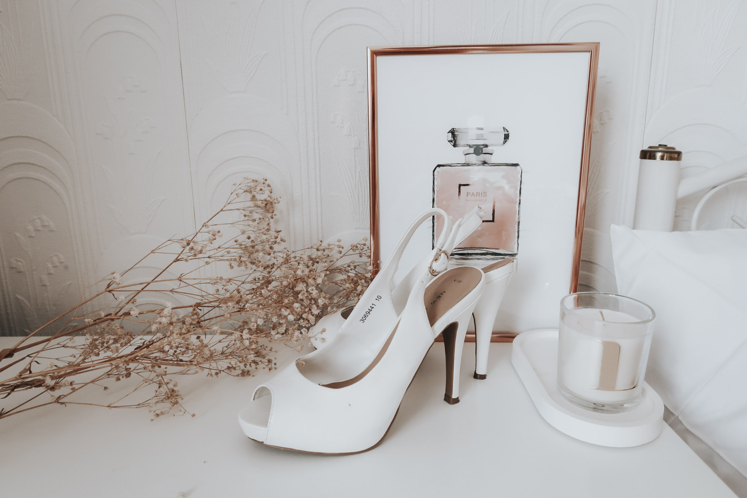 A pair of white high heels on a white chest of drawers.