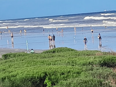 A foto mostra pessoas anônimas caminhando na praia em dia de maré alta.