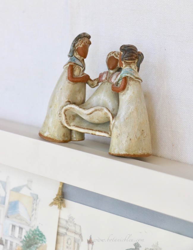 A handmade clay figurine is of three young French girls dressed in vintage clothing