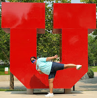 A martial arts black belt lady doing a side kick in front of the University of Utah
