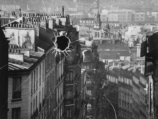 an André Kertész photograph 1929, a bullet hole in a window overlooking a city