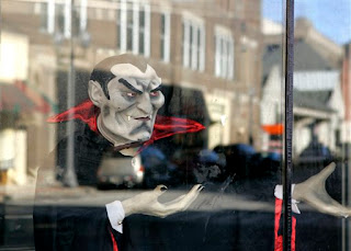 Buildings of downtown Oil City, Pa. are reflected in the windows of a Haunted House with a Dracula replica setup for the Halloween season