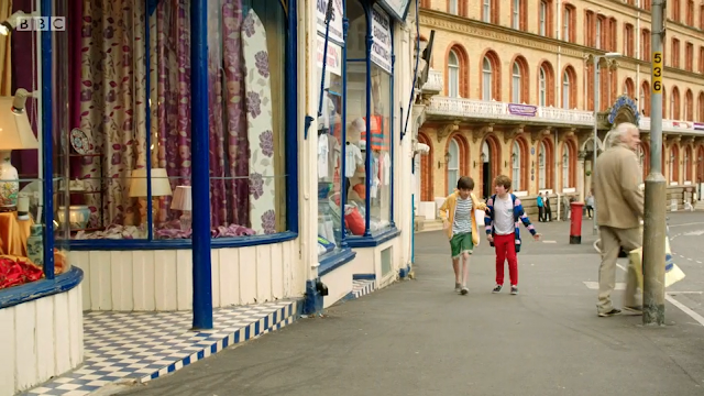 Two boys approach an antiques shop. Man by lamp post with shopping. St Nicholas Cliff, Scarborough. Grand Hotel entrance in background. From All at Sea Series 1 Episode 2.