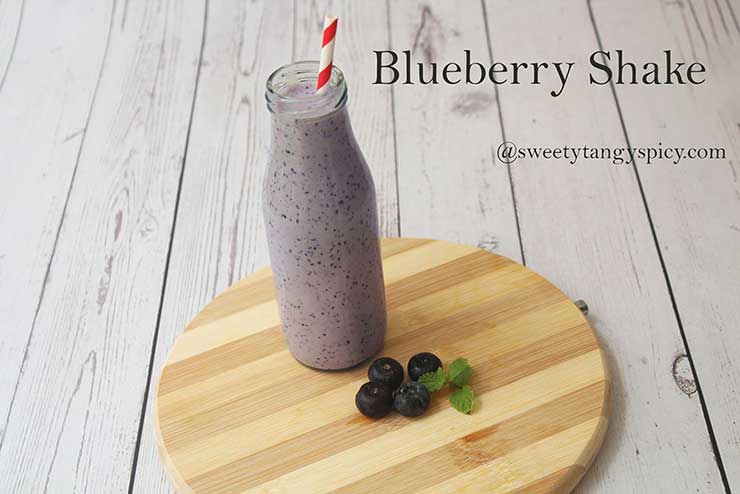 A glass filled with a creamy blueberry ice cream shake topped with whipped cream and fresh blueberries.