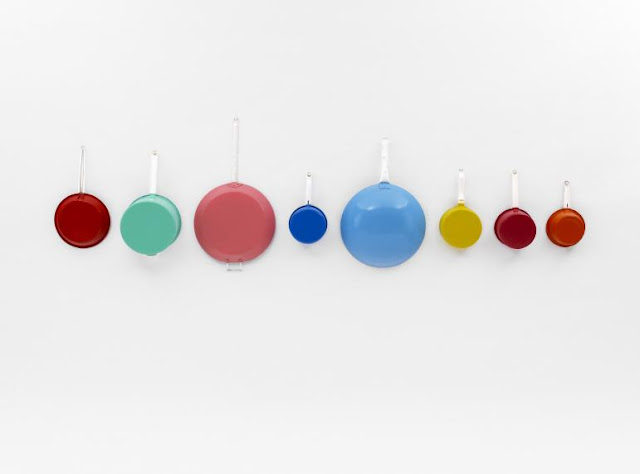 8 brightly painted colour saucepans on a white wall