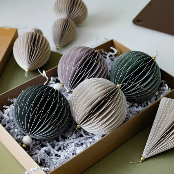 seven honeycomb paper ornaments in subtle shade displayed on flat surface, some in kraft paper box