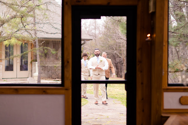 Summer and David decided on a small, intimate wedding, tying-the-knot at the tucked-away and woodsy Thunderbird Chapel in Norman, OK.  Little did Summer know when David became her personal trainer, that they would one day be married.  This was a second marriage for both, and Summer’s bridesmaid and maid of honor, and David’s best man were their respective children.    Summer was stunning in her trumpet style lace wedding dress, “killer” glittery heels, holding a beautiful, handmade bouquet consisting of pink roses, white lilies, pink freesia, white baby’s breath and greenery.  And David looked dashing in his champagne-colored, three-piece suit, light blue tie, and a single rose boutonniere. Such a beautiful couple on their wedding day!        Summer’s dad was brought to tears during his “First Look;” it was clear that this was a special day for him as well.  The littlest girls led the way down the aisle, dropping rose petals, and racing each other to the end, while David and his son watched with awe as Summer, his soon-to-be-bride, walked down the aisle, arm-in-arm with her dad.  The ceremony included the assembly of a Unity Cross, signifying the two becoming one together with their faith in Christ, and hand-written vows.  At the end of the ceremony, David, caught up in the emotion of the “I do’s,” kicked up his heel in celebration!     After the ceremony, the bride and groom were greeted by a throng of well- wishing guests blowing bubbles.  The day was filled with heartfelt moments shared by the people they loved, and we tried our best to capture every beautiful detail, big and small.