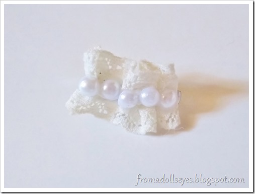 A hair accessory for a doll make with a scrap of gathered lace and some flat back pearls glued down the center.