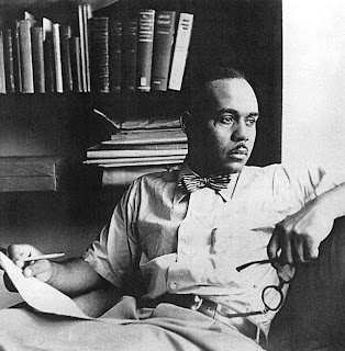 African American writer Ralph Ellison in front of a bookcase