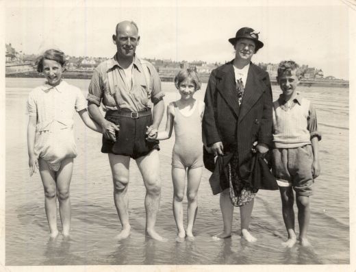 A family in the sea with water up to their ankles, with their clothes hoisted up so they don't get wet