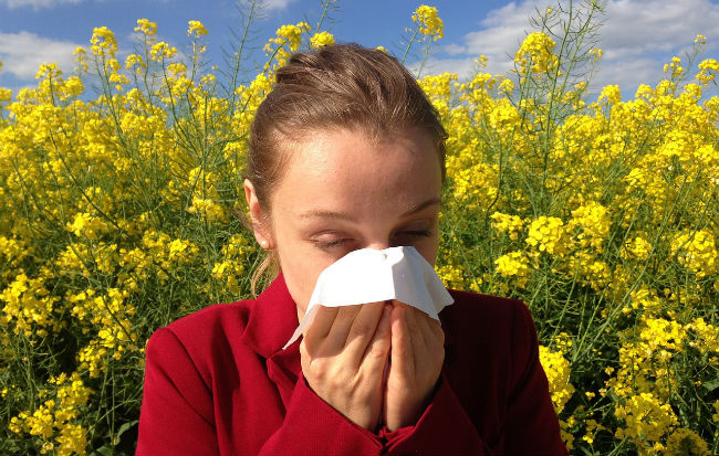 Donna allergica tra i fiori che si soffia il naso