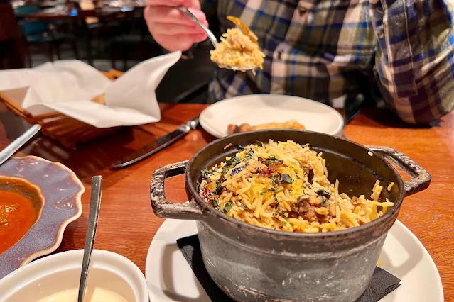 A small cast iron casserole dish with chicken biryani in on a table surrounded by other food