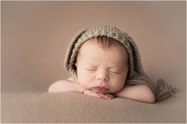 Sleeping baby with chin on folded hands wearing a knitted hat on a brown background