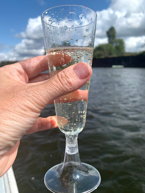 hand holding glass of prosecco on boat with view of river