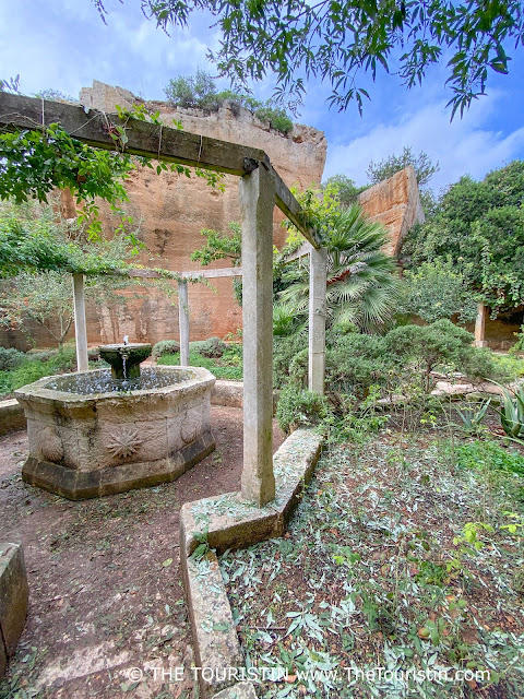 A sandstone fountain filled with water surrounded by the remnants of giant sandstone quarries overgrown by lush greenery.