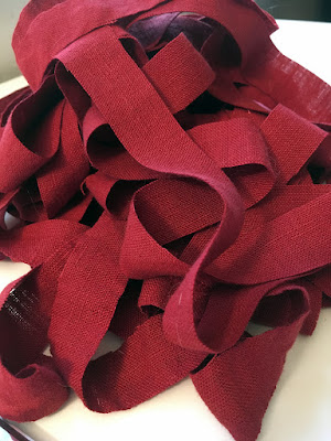 A pile of narrow red linen strips with clean cut edges on a white table. They look like surreal linguine.