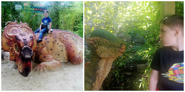 Sitting on a large dinosaur model and face to face with a smaller one. 