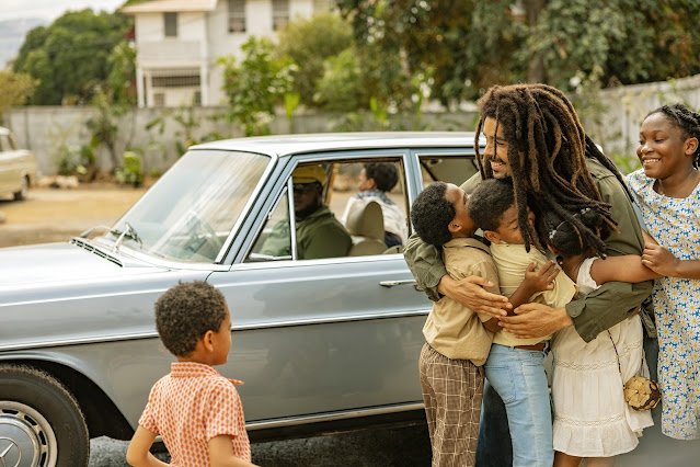 A man returning home hugs his children by a car
