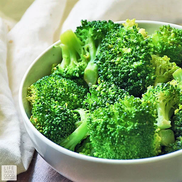 Vibrant green steamed broccoli in a white bowl. Learn how to steam broccoli so it is crisp and retains the green color