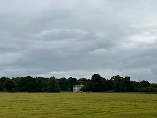 A view over some fields to a mansion house in the distance.  Trees grow on either side of the house.  Photograph by Kevin Nosferatu for the Skulferatu Project.