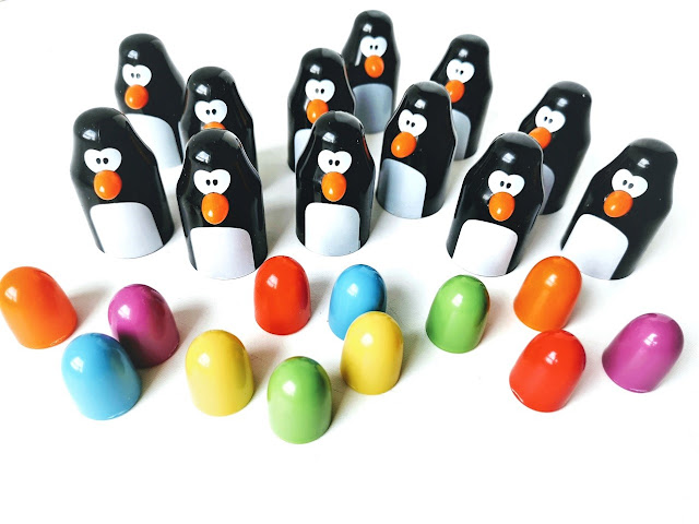 na zdjęciu widac dwanaście pingwinów i ustawione przed nimi dwanaście jajek o dwa w kolorach czerwonym, pomarańczowym, niebieskim, zielonym żółtym i fioletowym