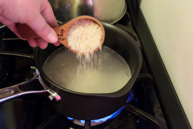 Uncooked rice being added to the boiling water in the sauce pot. 