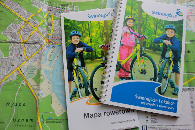 Mapa i mały przewodnik rowerowy,przygotowane przez Biuro Informacji Turystycznej w Świnoujściu. Foldery promocyjne ze zdjęciem jadących na rowerach dzieci leżą na tle planu Świnoujścia.