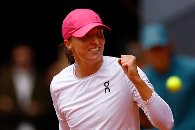 Iga Swiatek está de boné rosa e camisa branca, comemorando ponto. Ela é branca e está sorrindo