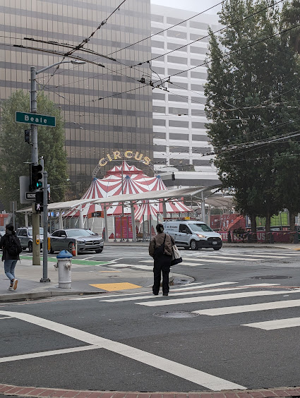 Foggy morning; two office building in the distance, crosswalk in the foreground, a red and white circus tent in the middle ground