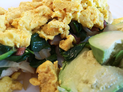 Scrambled eggs and spinach on an English muffin with avocado