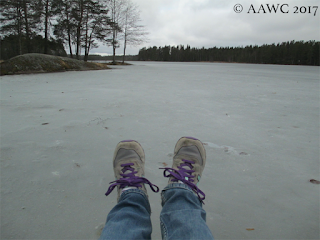 A lake that has been frozen over, with someone's feet lying on the ice.