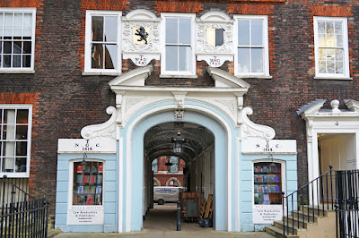 The ground and first floors of part of a Georgian brick building with sash windows. In the centre is an alley passing through the building, with a stucco frontage including a split pediment and scrolls painted white, and a light blue-painted frontage with two windows displaying law books.