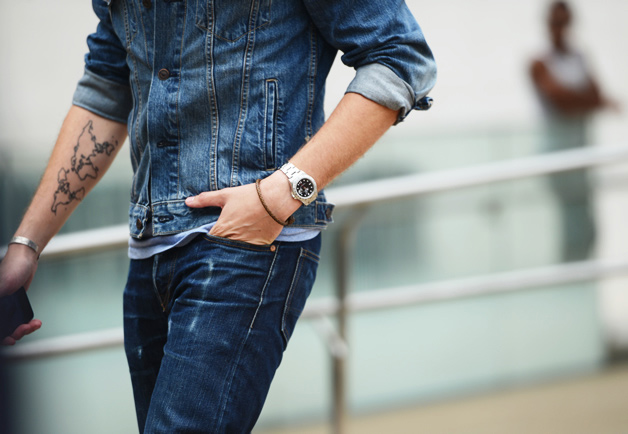 This picture is showing a tattooed man wearing bracelet and watch in his hand.