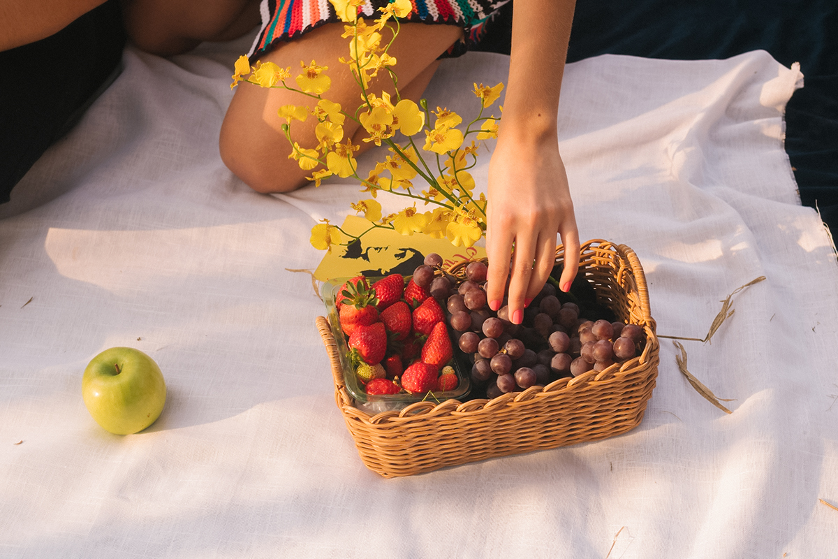 female's hand reaching into a basket with fresh fruits