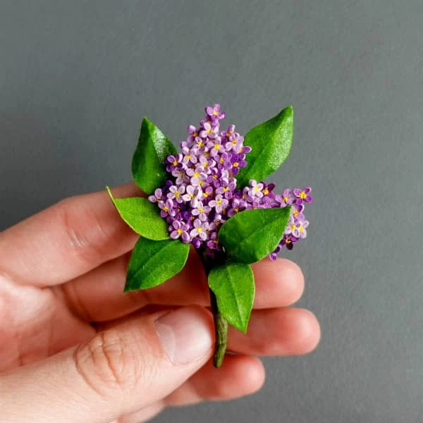 fingers holding quilled purple lilac blossoms with green leaves made with very narrow quilling strips