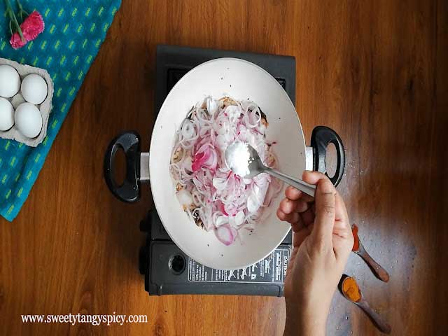 Thinly sliced onions being added to the pan along with a pinch of salt, a key step in crafting Kerala Egg Roast.