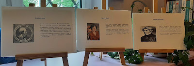 Zdjęcie przedstawia trzy sztalugi. Na pierwszej znajduje się zdjęcie Eratostenesa wraz z krótką biografią . Na drugiej sztaludze znajduje się zdjęcie Laury Bush oraz jej krótka biografia. Na trzeciej sztaludze znajduje się zdjęcie Adama Mickiewicza wraz z krótką biografią.
