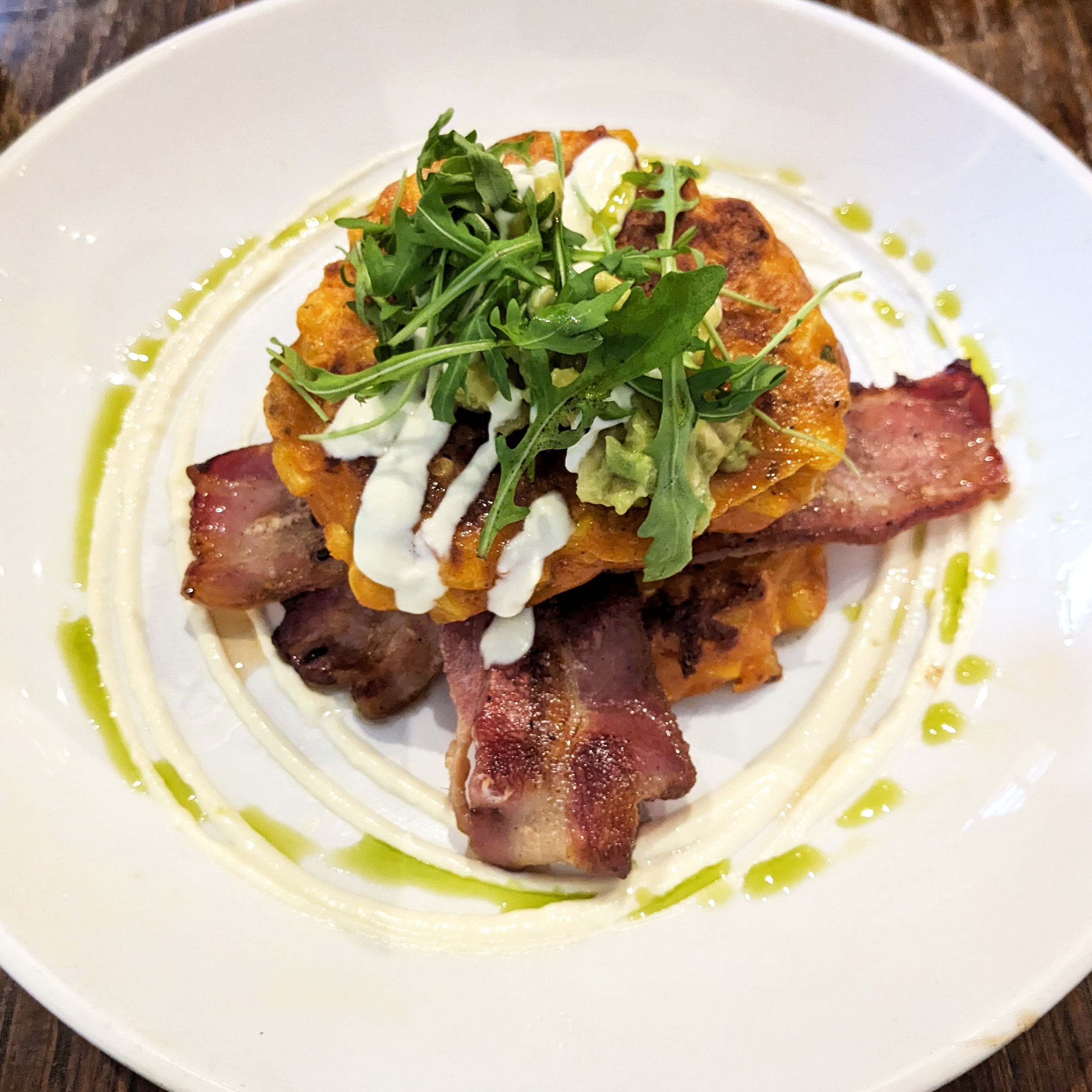 A large white plate filled with sweetcron fritters, streaky bacon, spinach and avocado at Lantana London, one of the best brunch places in London Bridge