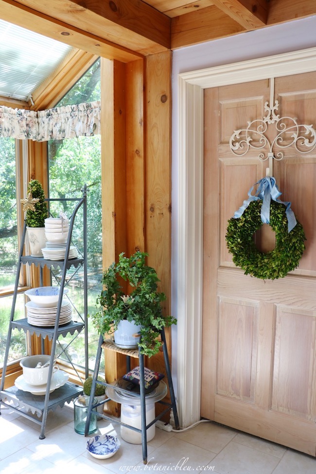 White every day dishes are stored on a French-style shelf in a French Country inspired conservatory.