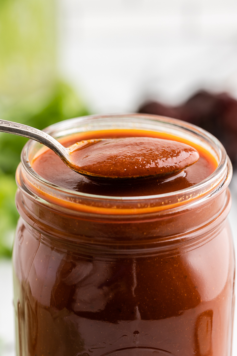 Closeup of a spoonful of Homemade Red Enchilada Sauce over a mason jar full of it.