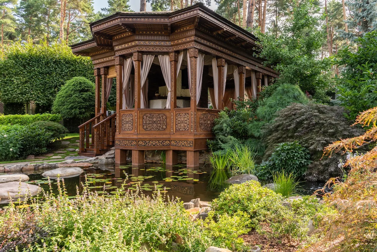 brown wooden gazebo surrounded by green trees and a pond