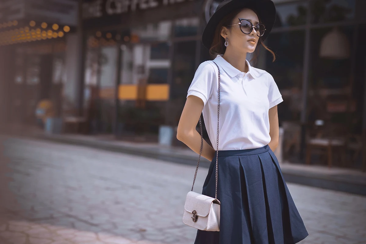 beautiful woman in a white athletic polo shirt and skirt is posing on a street