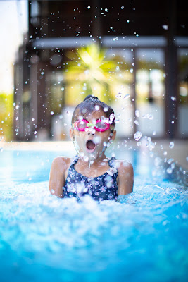 Picture of a child jumping into the water with an open mouth showing her surprise. Why Year-Round Swimming is Important.