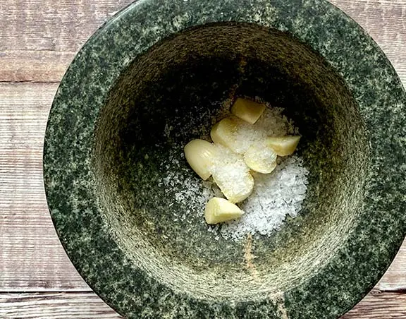 Garlic in a pestle and mortar with salt and sugar.