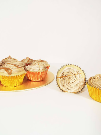 Picture of two cinnamon spiced biscoff cupcakes lying next to each other, adjacent to gold plate with other various gold and copper wrapped cinnamon spiced cupcakes huddled together.
