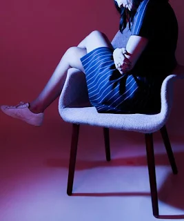 A depressed woman sitting on a chair and holding herself.