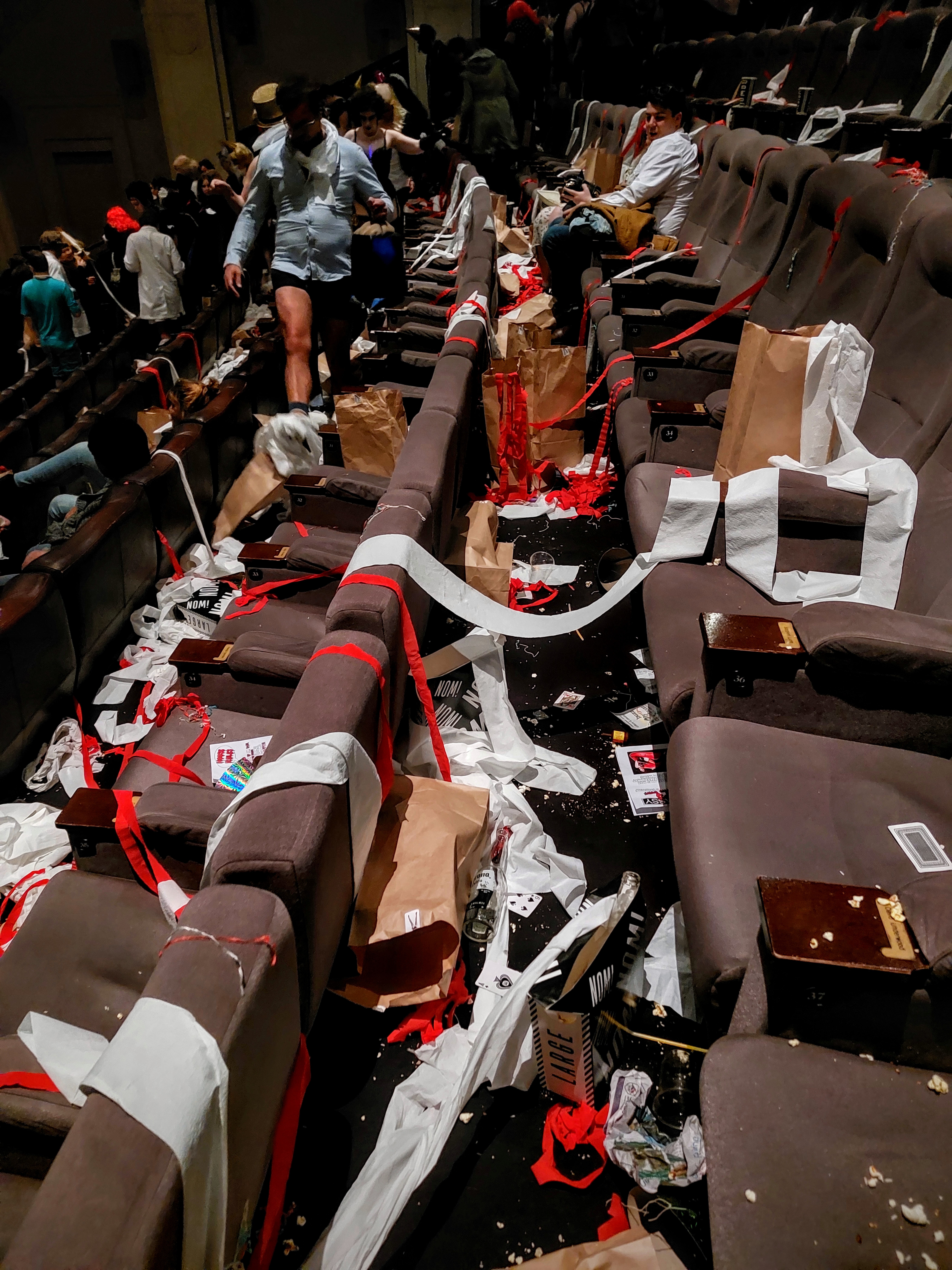 Cinema rows of seats covered in thrown toilet paper.tolls and other Rocky Horror audience interaction goodies. Some people in costume are leaving in the background. Fun!